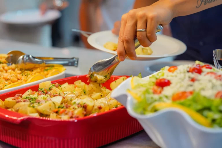 Mão se servindo na pista de refeições de restaurante corporativo.